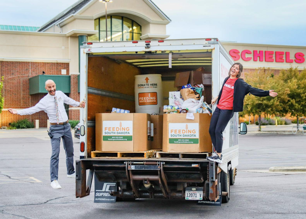 Two scheels employees on the back of a Feeding south dakota truck filled with donated food