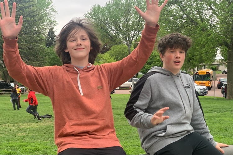 two students with arms up sitting on a bike rack