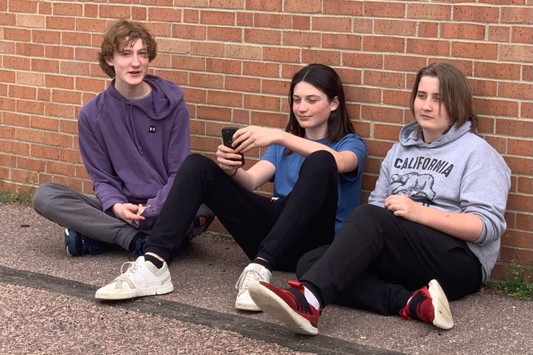 three students sitting against the wall talking and laughing